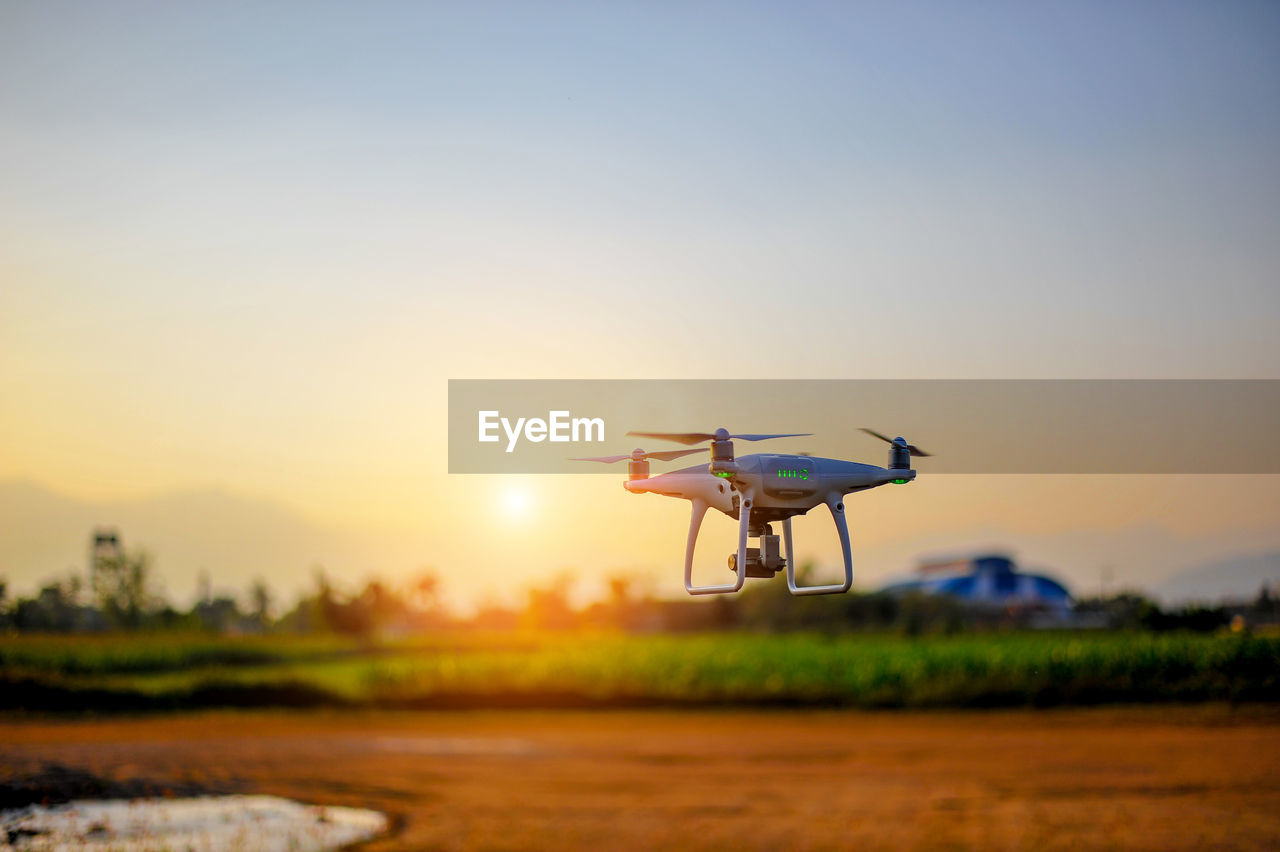 Drone flying against sky during sunset