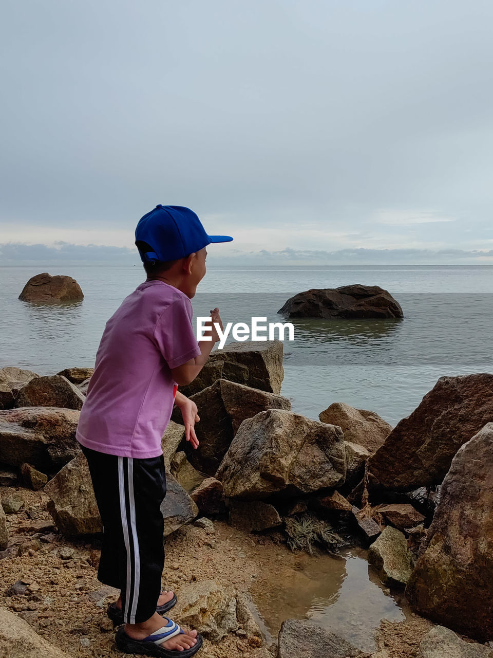 water, sea, rock, one person, beach, land, coast, shore, ocean, sky, full length, nature, hat, adult, beauty in nature, standing, leisure activity, body of water, side view, scenics - nature, casual clothing, vacation, bay, men, horizon over water, lifestyles, clothing, day, outdoors, holiday, cap, child, childhood, horizon, trip, looking, women, wave, tranquility, sand, activity, female, cloud