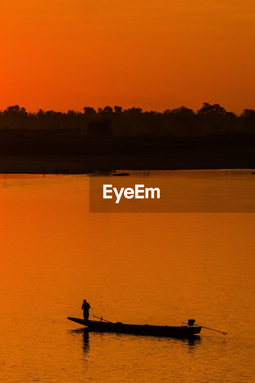 Silhouette person on lake against orange sky