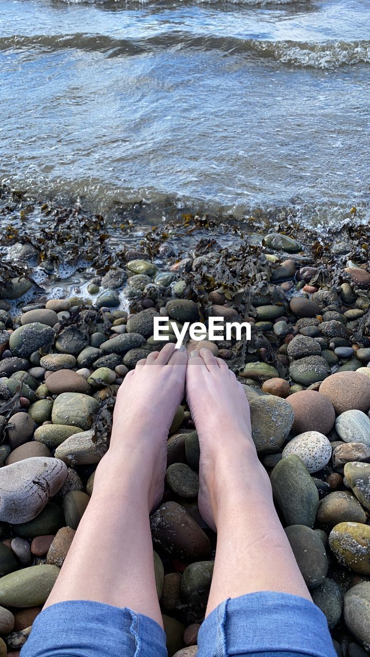 LOW SECTION OF PERSON LEGS ON ROCK AT BEACH
