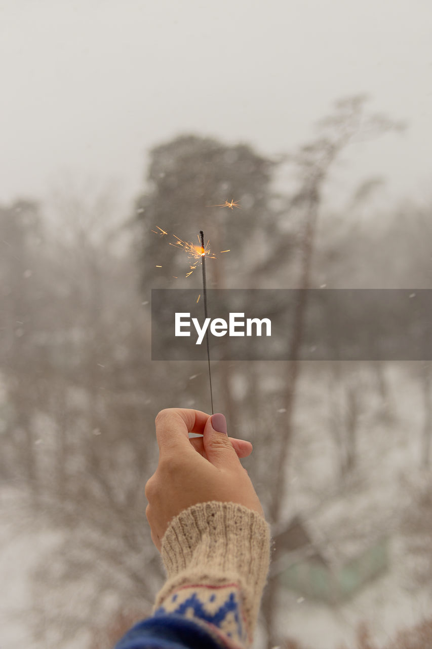 Woman's hand holds sparkle during snowfall with views of nature and houses