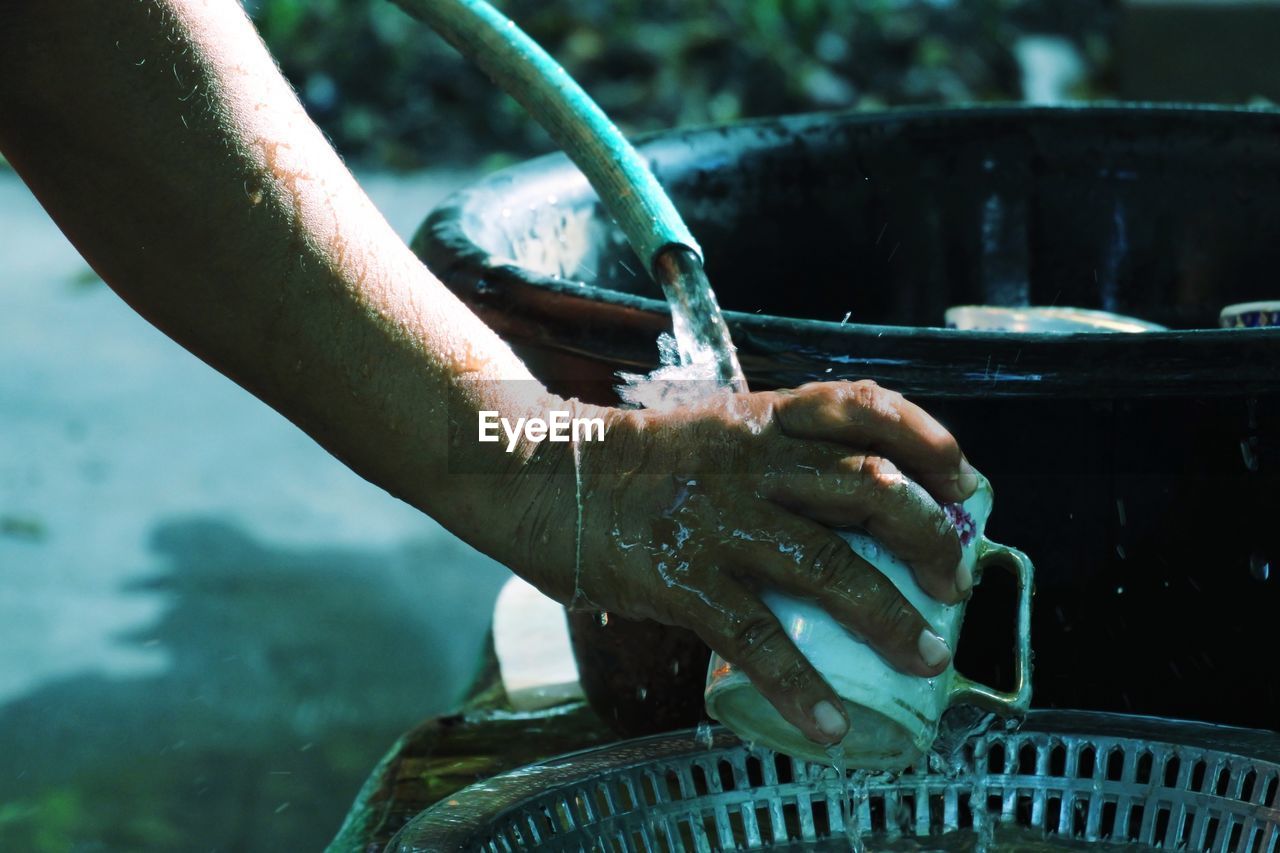 Cropped hands of person cleaning utensils with water