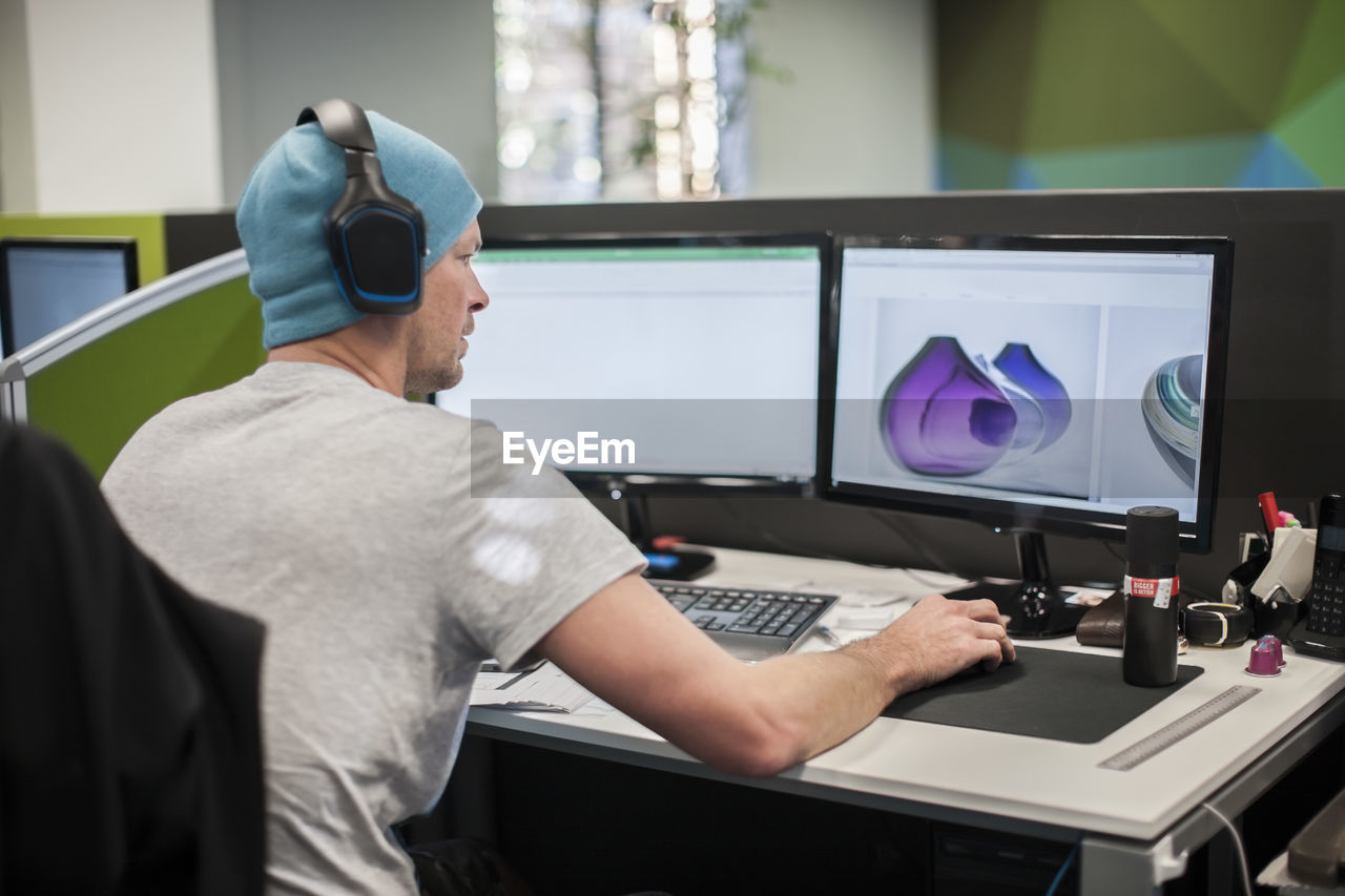 Young man wearing headphones working on computer in office