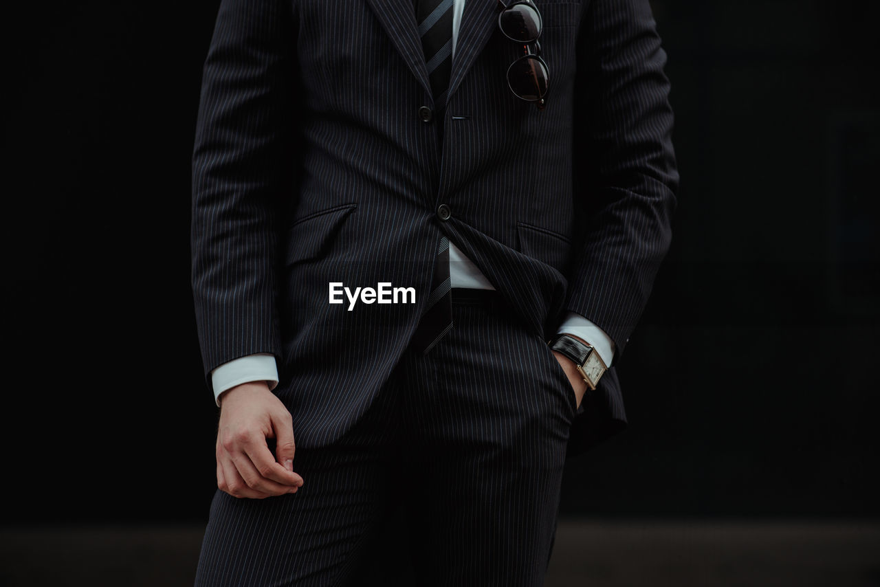 MIDSECTION OF MAN STANDING IN FRONT OF BLACK BACKGROUND