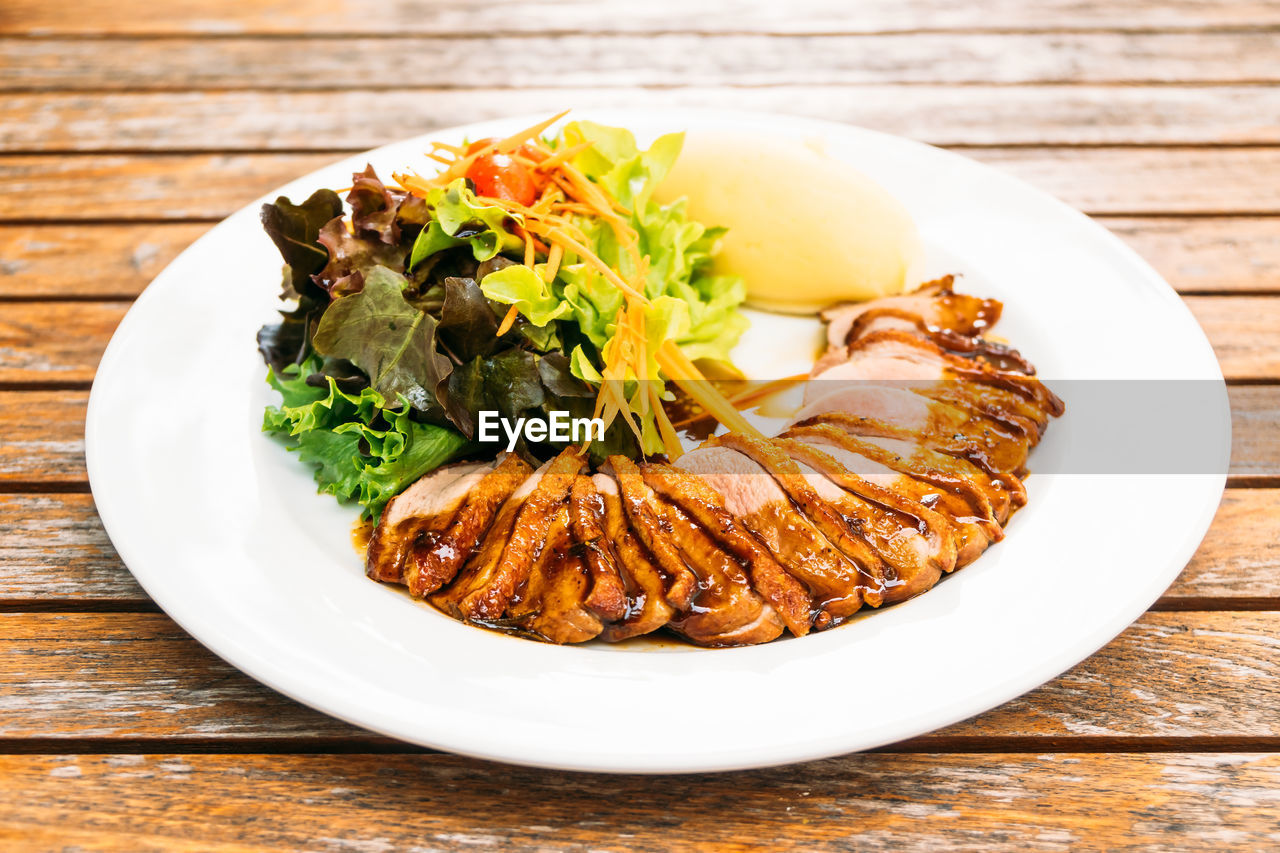 High angle view of roasted meat and salad in plate on table