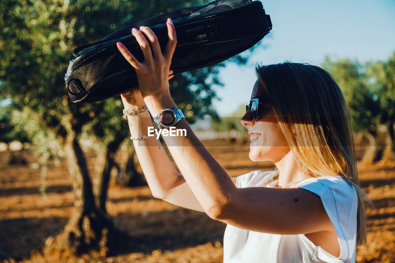 Side view of woman shielding eyes while standing at olive orchard