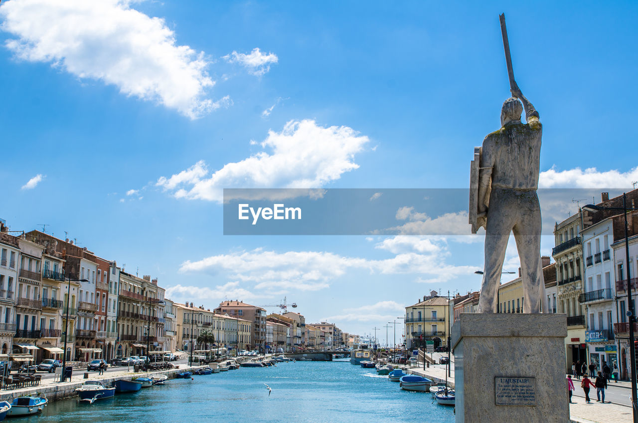 Statue by canal in city against sky