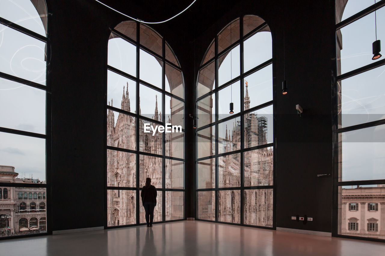 Woman looking at milan cathedral through glass window