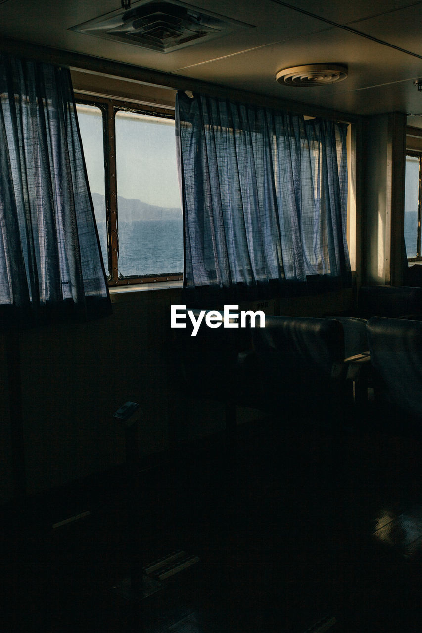 The passenger seats on the ferry boat, view through the window and curtains  behind which is sea.