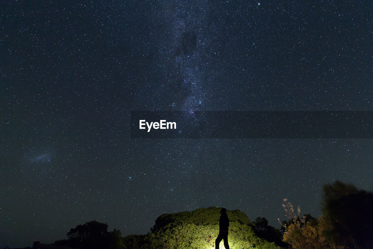 Silhouette man walking by trees against star field at night