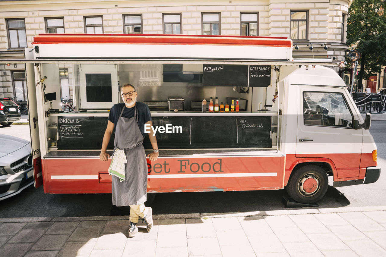 Full length of male chef standing against food truck at city street