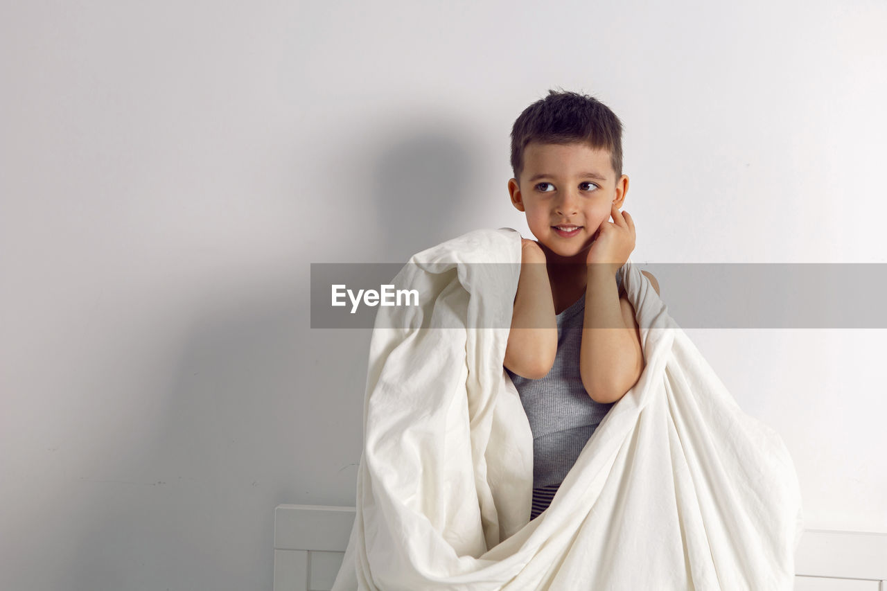 Child boy is mad having fun in a white bed in the children's room with a blanket