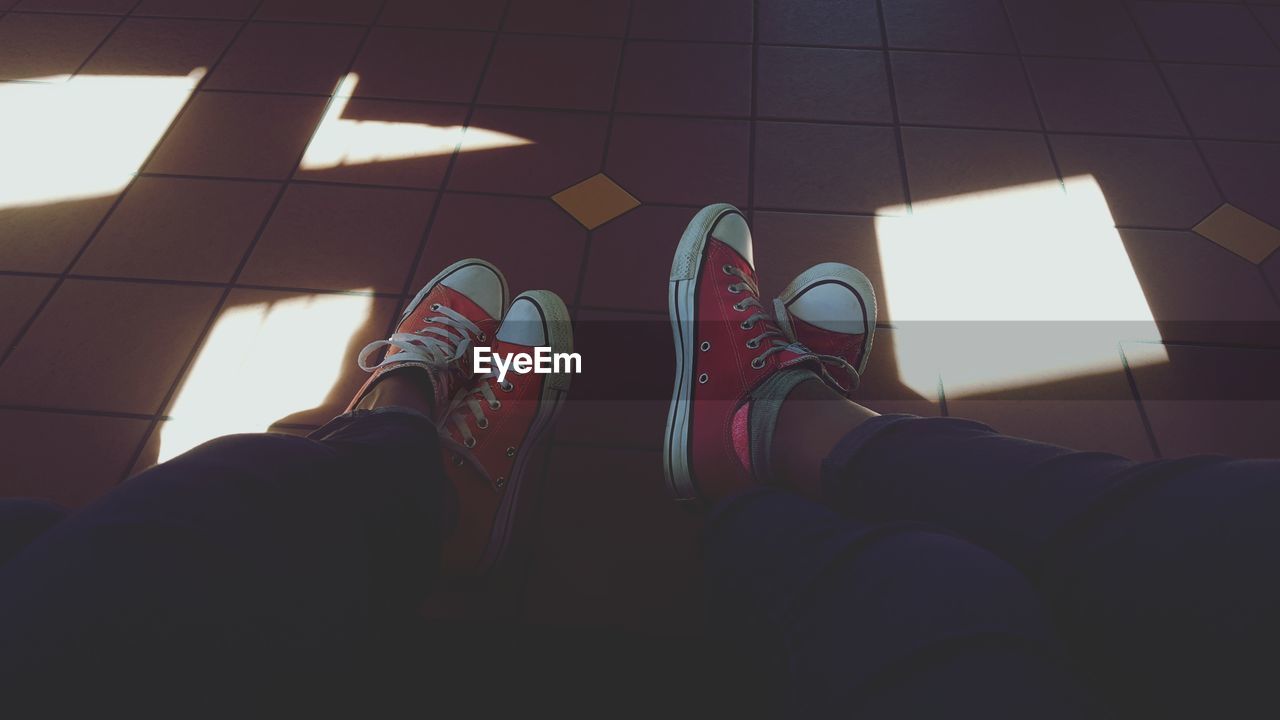 Low section of friends wearing red canvas shoes on tiled floor