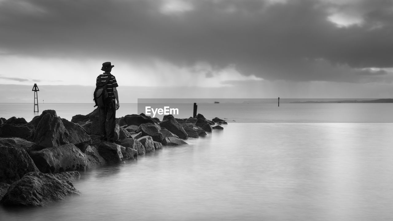 Man standing on rock in sea against sky