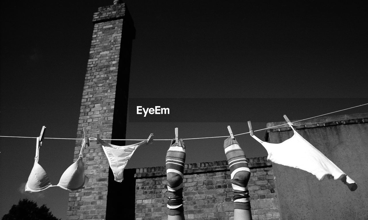 Cropped image of person wearing socks hanging with lingerie against building