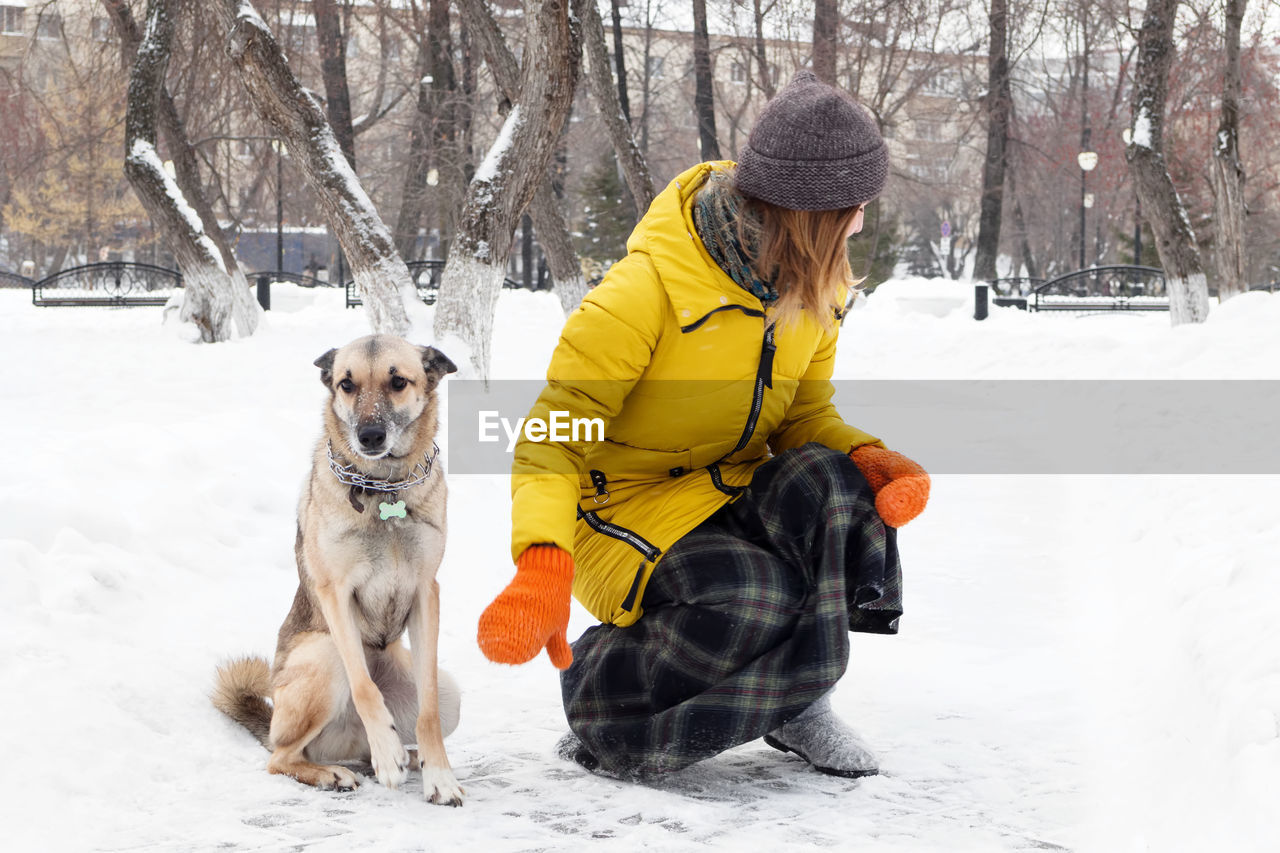 Young woman is walking with her dog in a snowy winter park.