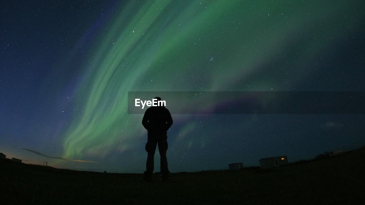 Rear view of silhouette man standing against aurora polaris