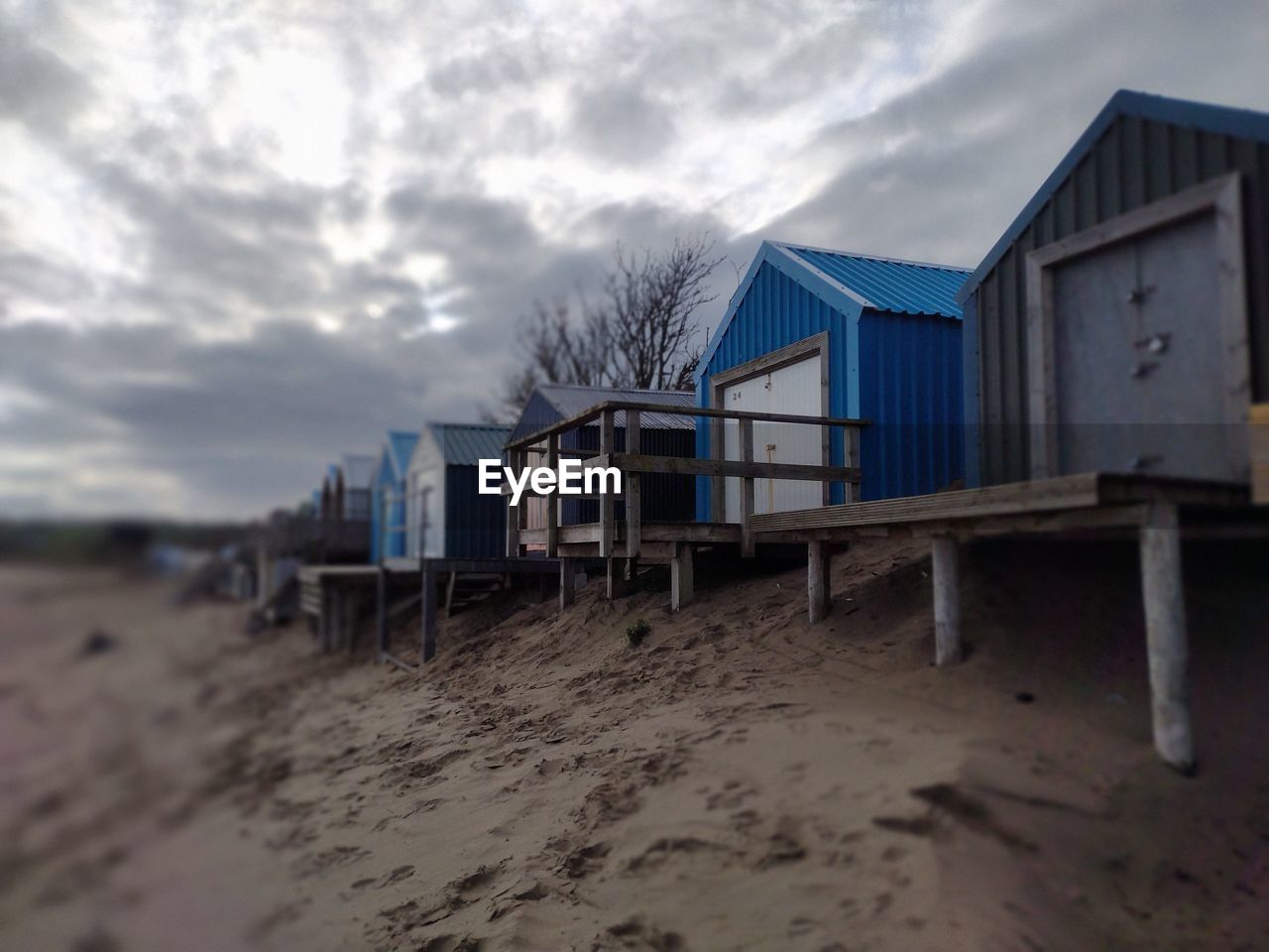 cloud, sky, architecture, sand, built structure, beach, land, hut, nature, building exterior, building, no people, water, outdoors, house, beach hut, sea, day, wood, stilt house