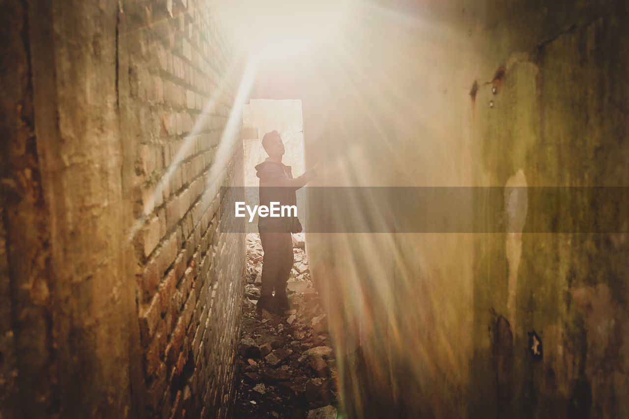 REAR VIEW OF MAN STANDING AGAINST SUN SHINING THROUGH SUNLIGHT