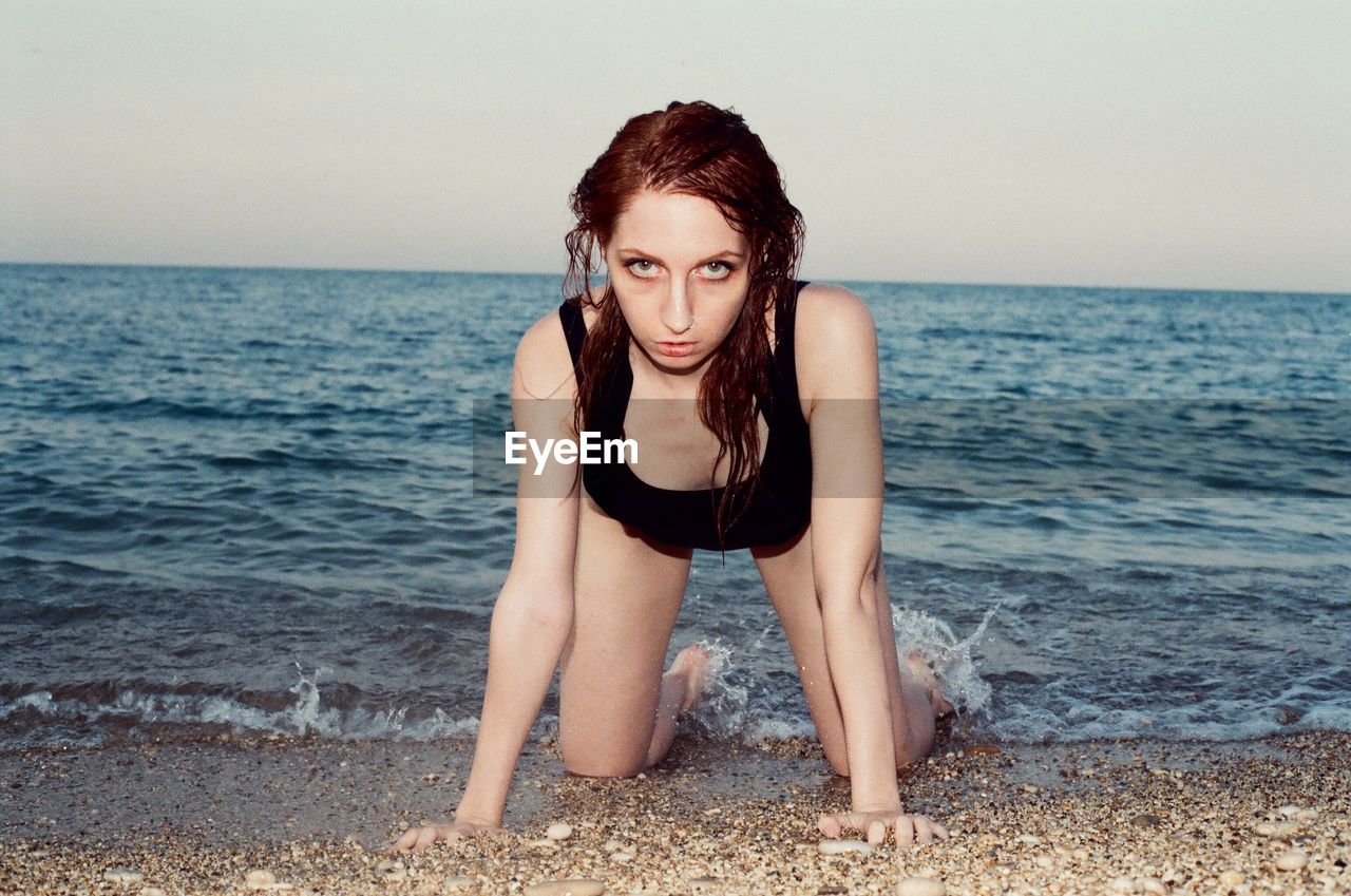 Portrait of woman kneeling at beach against clear sky