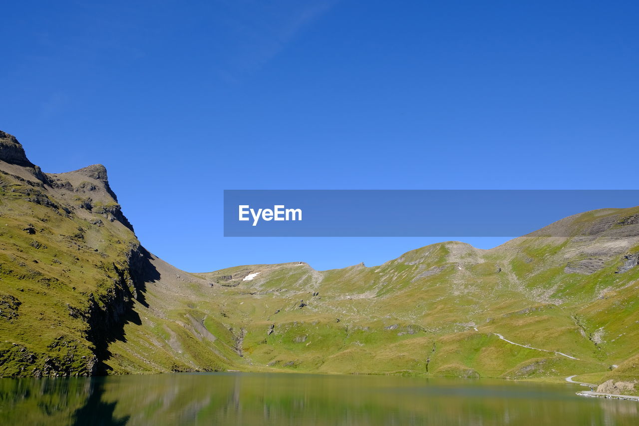 Scenic view of lake and mountains against clear blue sky