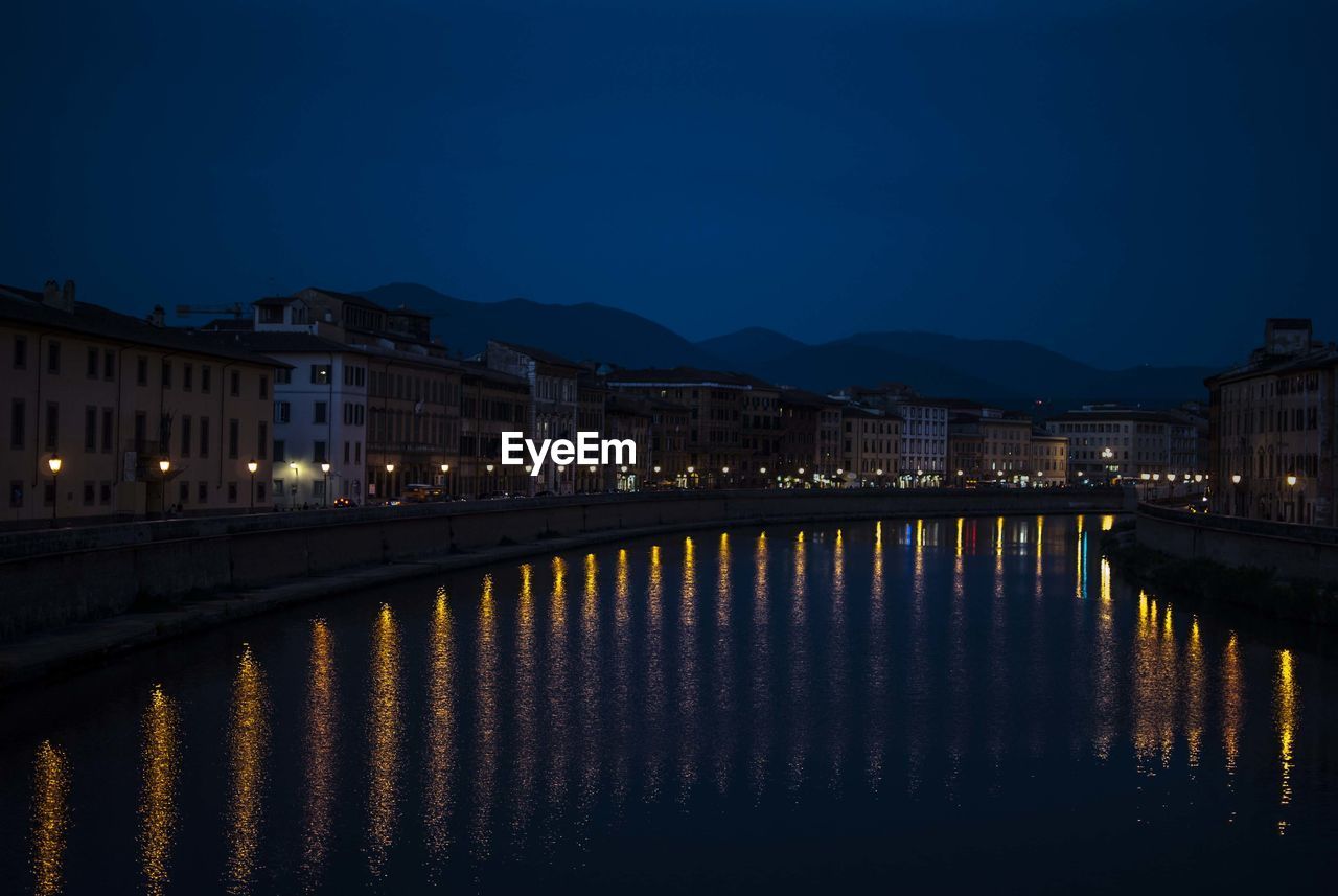 Illuminated buildings by lake against sky at night