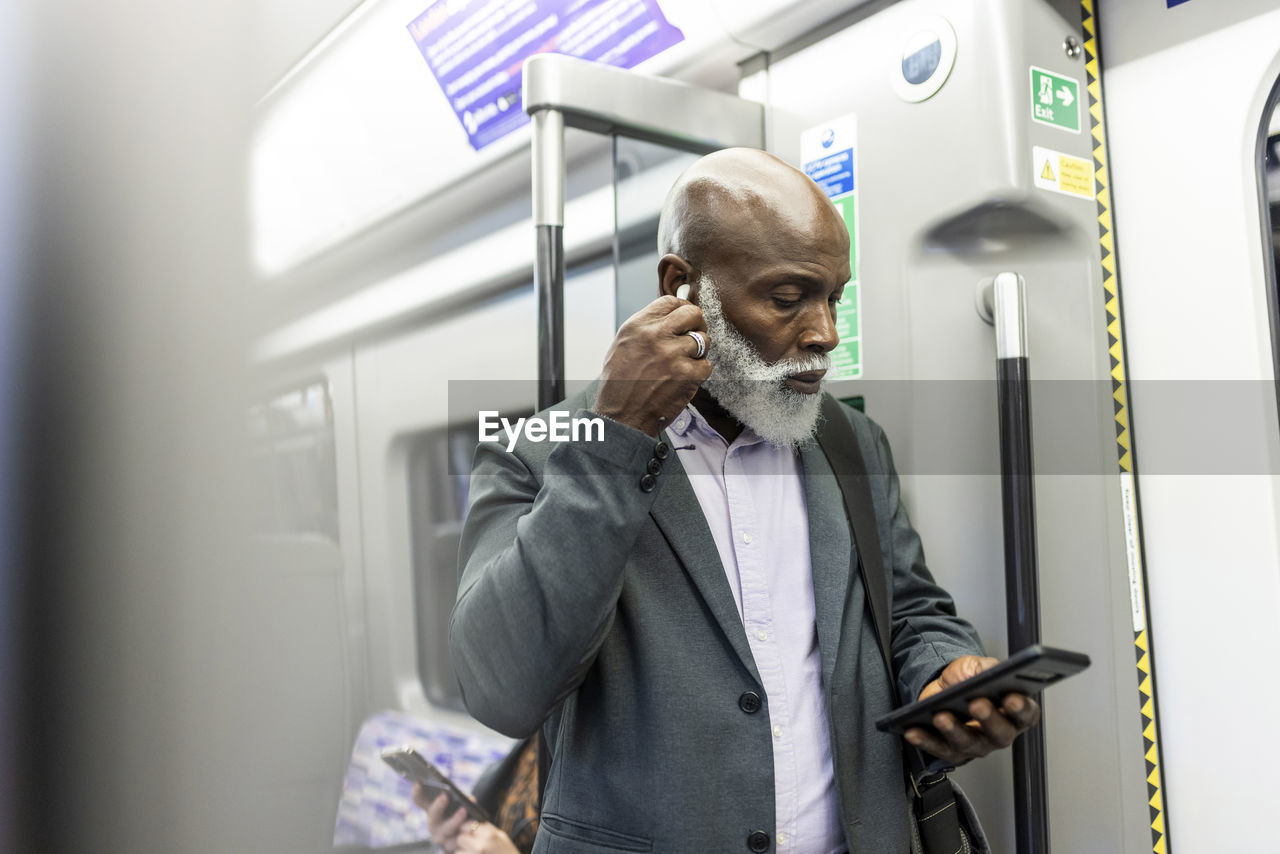 Businessman with smart phone wearing wireless in-ear headphones in train
