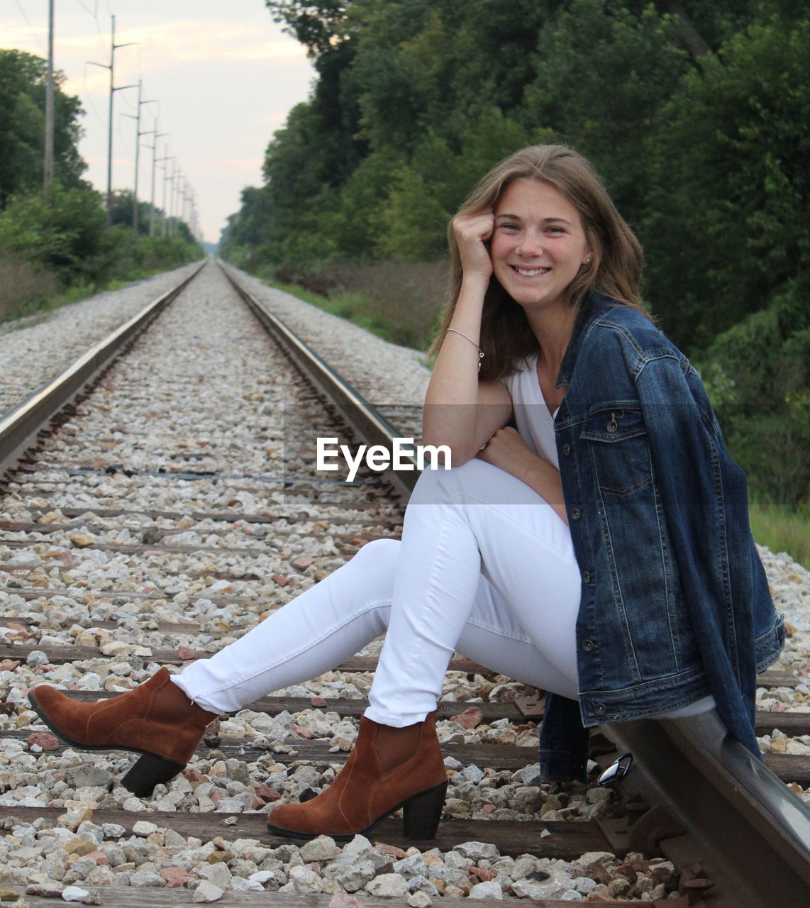 Full length portrait of smiling young woman sitting on railroad track