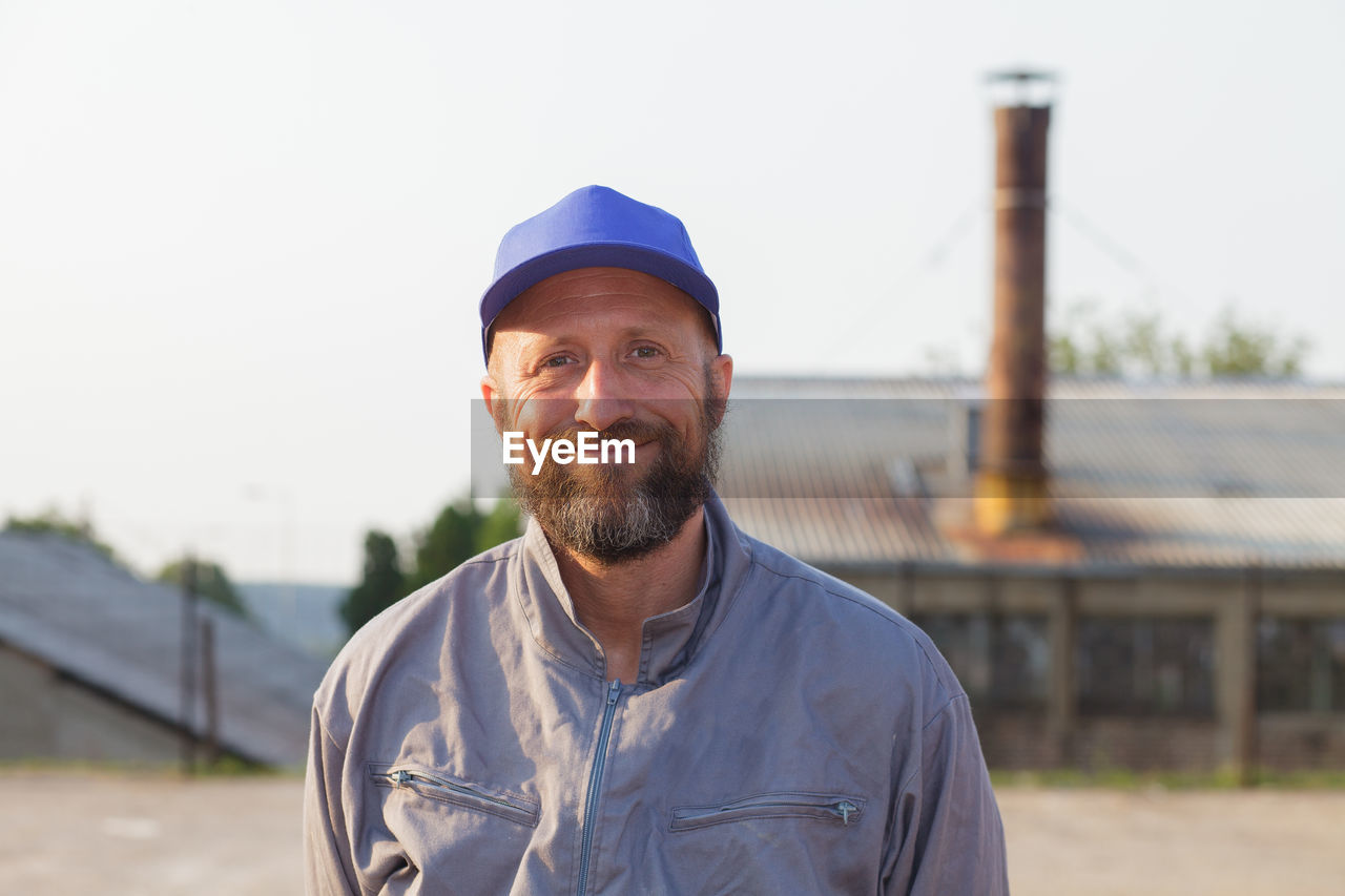 Portrait of smiling worker standing by factory against clear sky