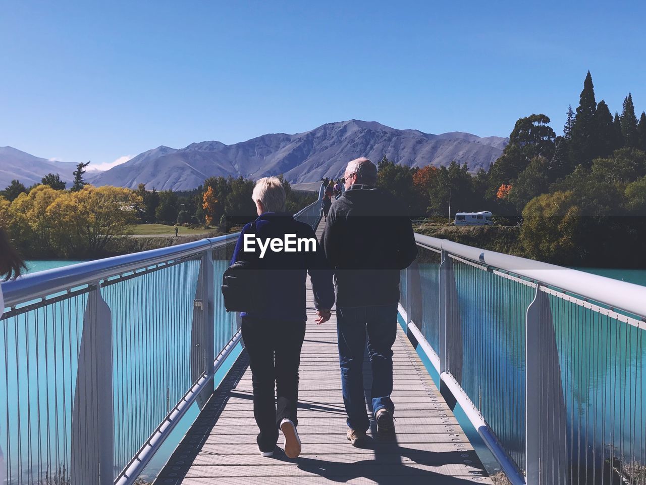 Rear view of people walking on footbridge against clear sky