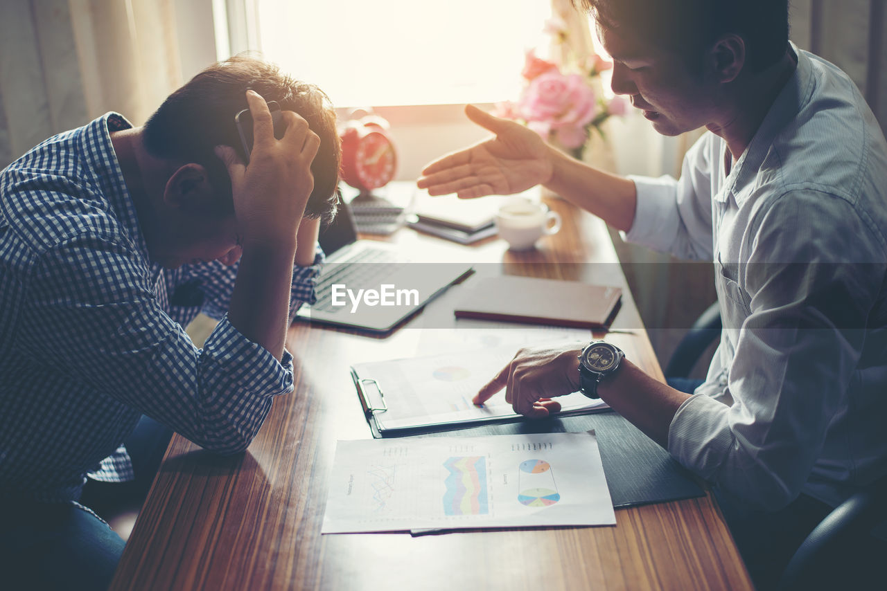 Side view of businessman discussing graphs with frustrated employee on desk in office