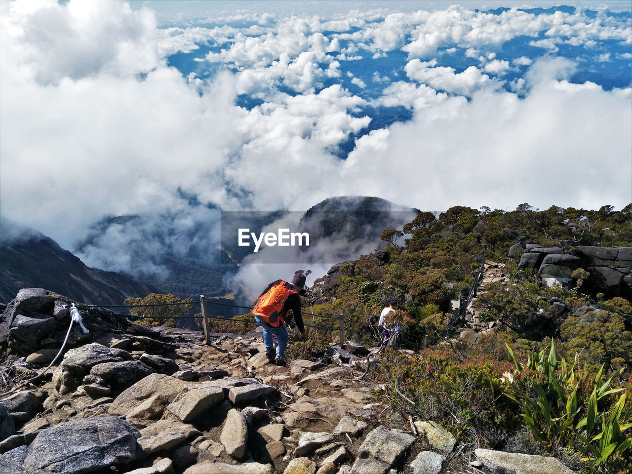 Rear view of hikers walking on mountain against cloudy sky