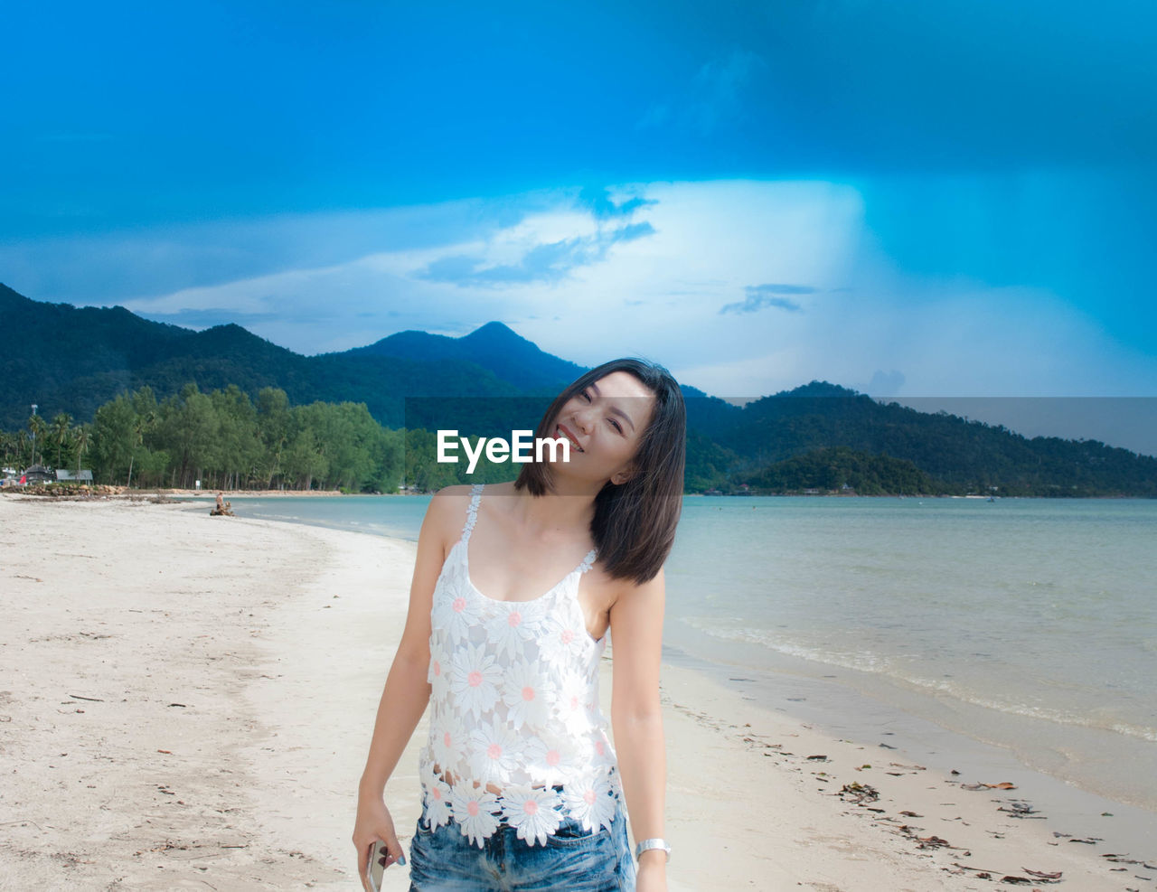 Portrait of smiling mid adult woman standing on beach against blue sky