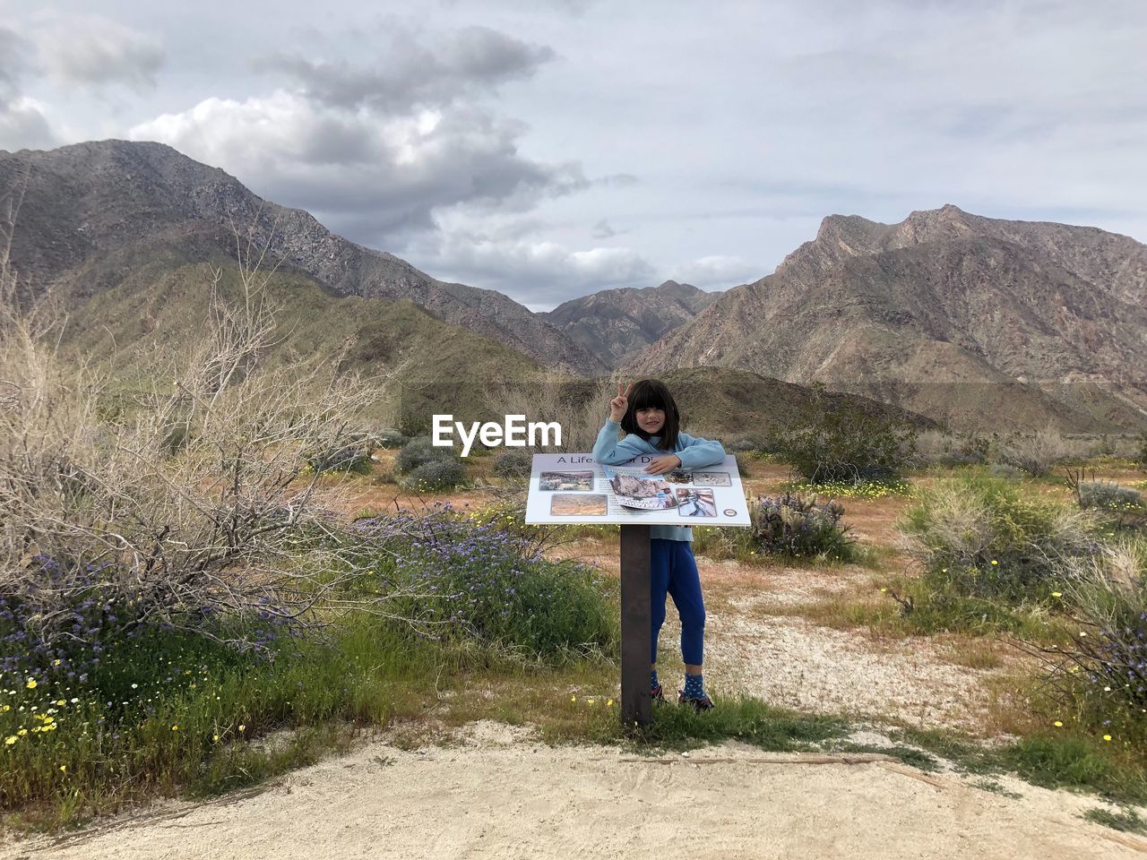 Full length of girl standing by information sign on land against mountains