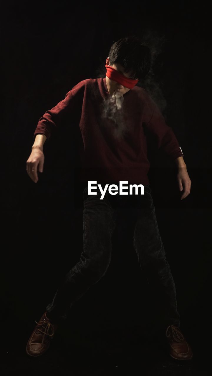 Blindfolded man smoking while standing against black background