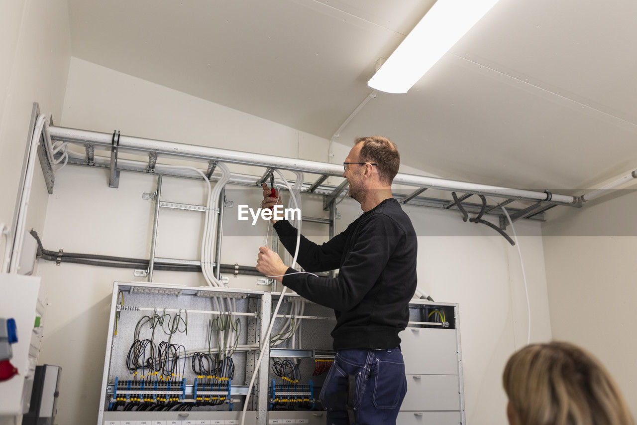 Male technician fixing cable wires on ladder in meter room