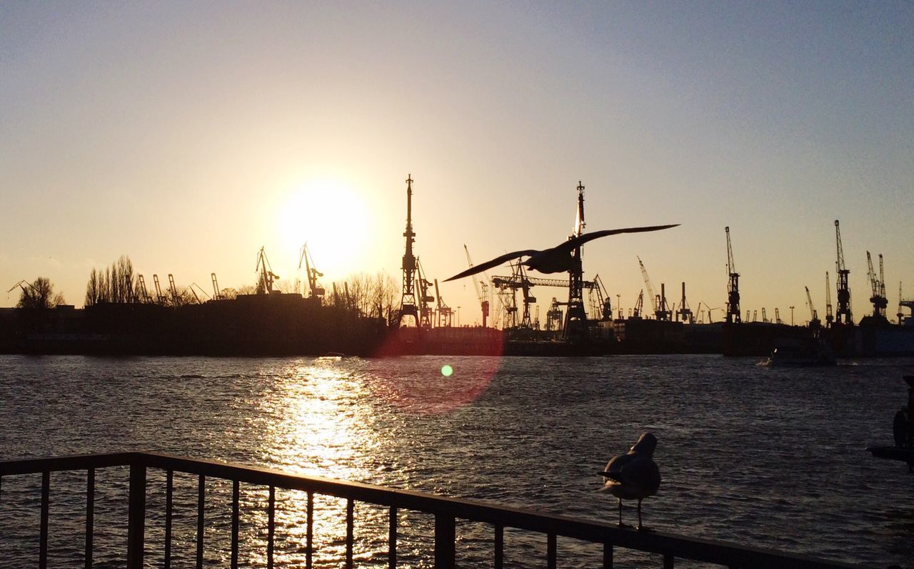 Silhouette cranes at commercial dock against clear sky