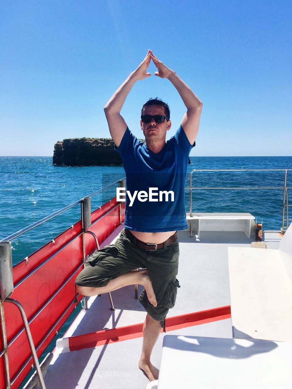 Full length of young man doing yoga while standing on boat at sea against sky