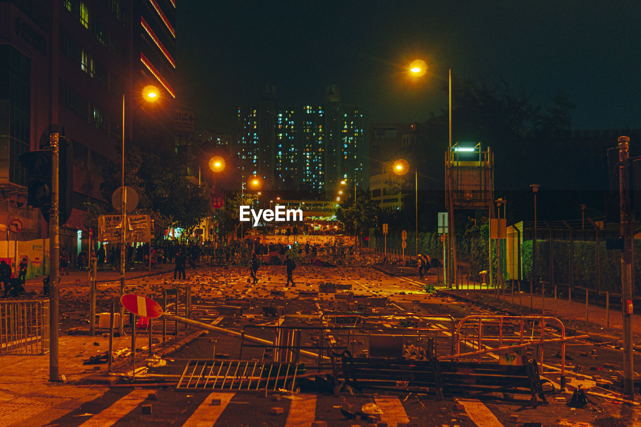 Illuminated street amidst buildings against sky at night