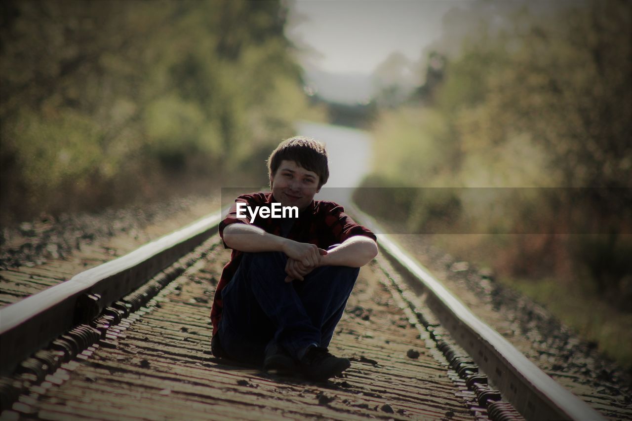 Portrait of teenage boy sitting on railroad track