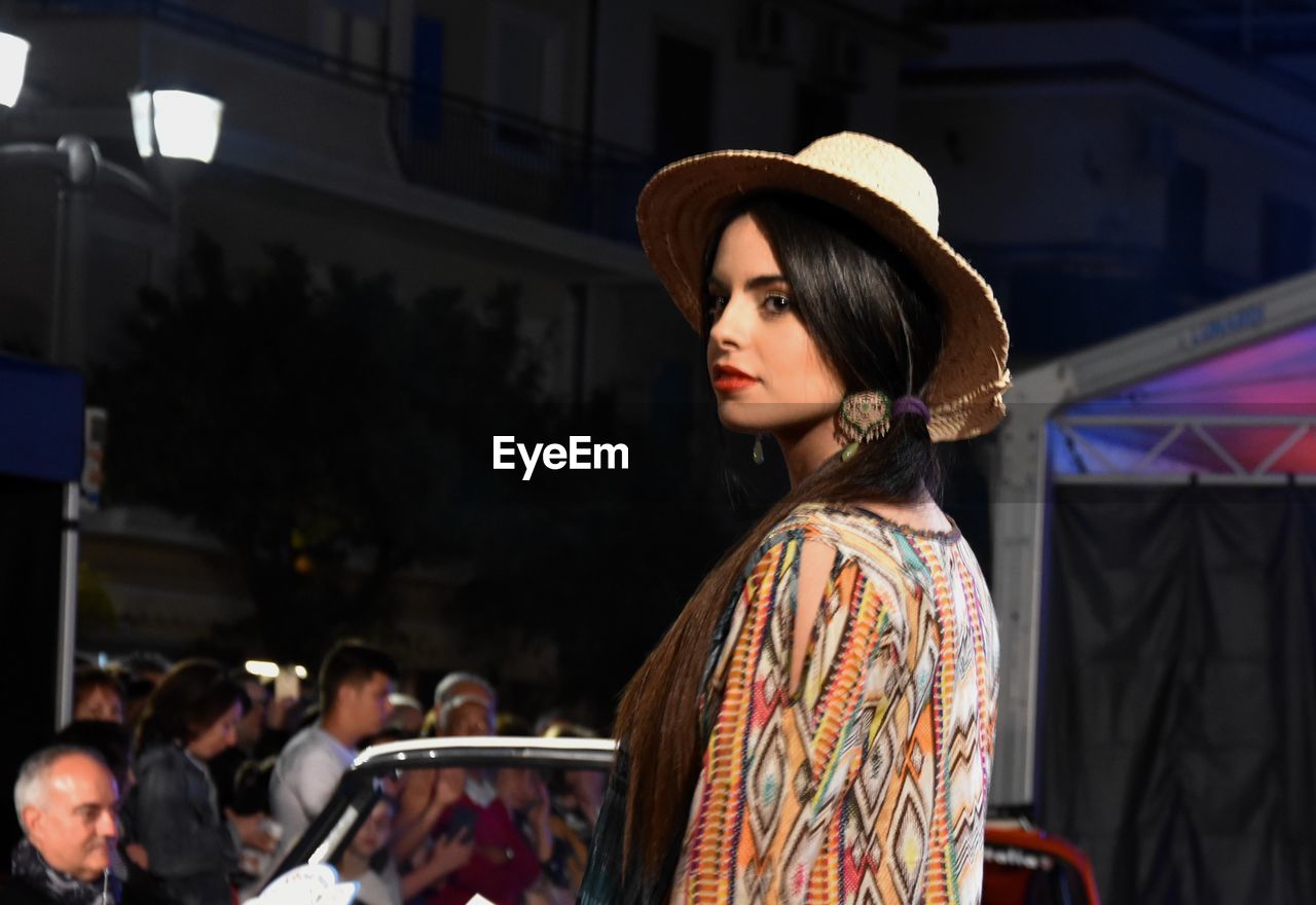 PORTRAIT OF YOUNG WOMAN LOOKING AWAY WHILE STANDING AGAINST BUILT STRUCTURE