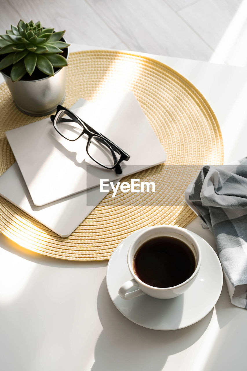 Office desk with coffee cup, succulent plant, eyeglasses and notepad.