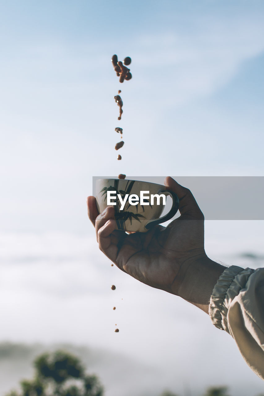 Midsection of person holding coffee cup against sky