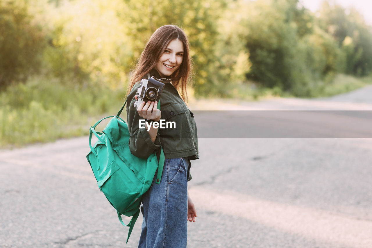 A beautiful girl with a camera in her hands is walking along the road in search of interesting shots