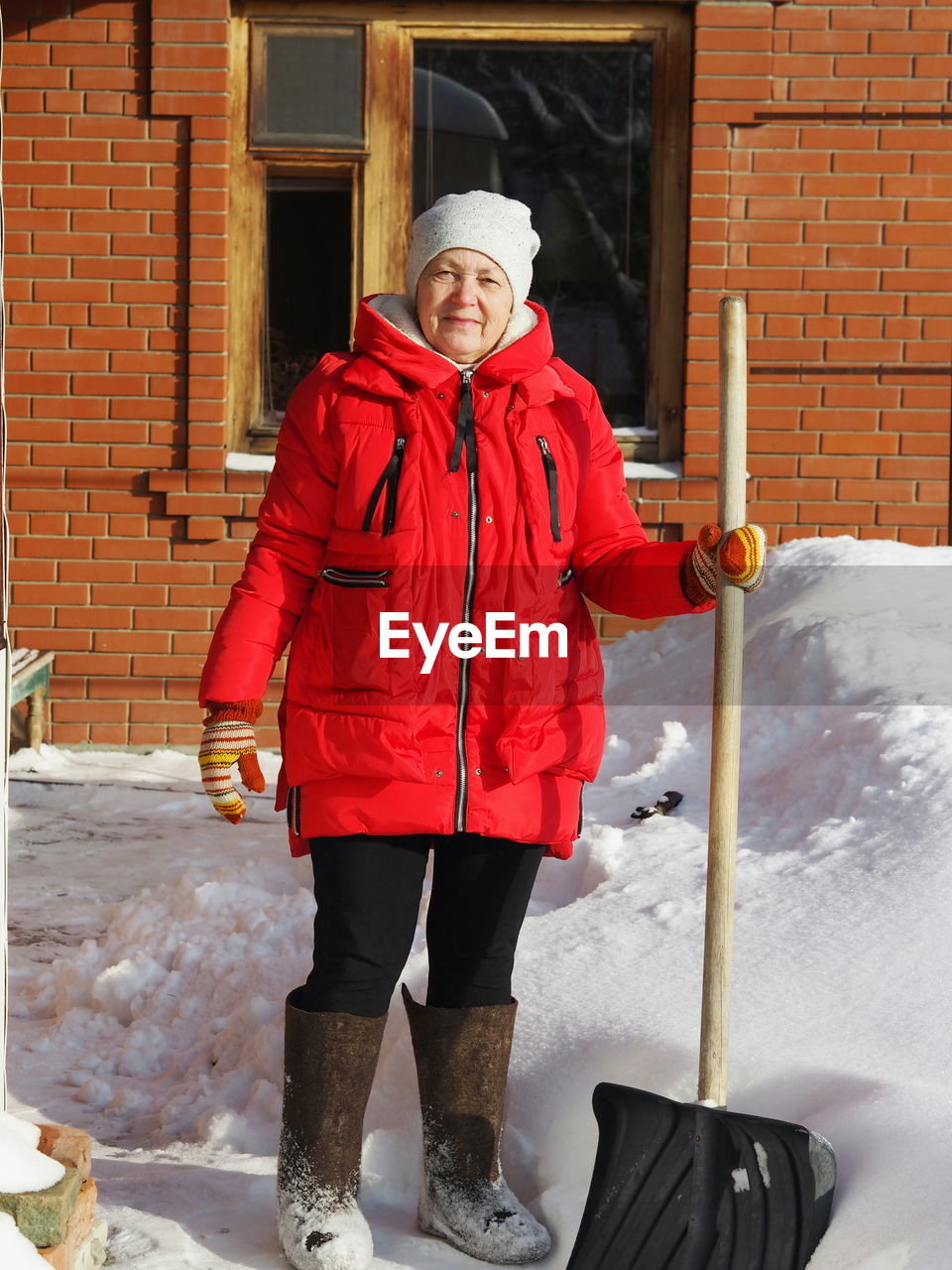 A woman with a shovel to clear snow near a private house. snow removal from the territory. 