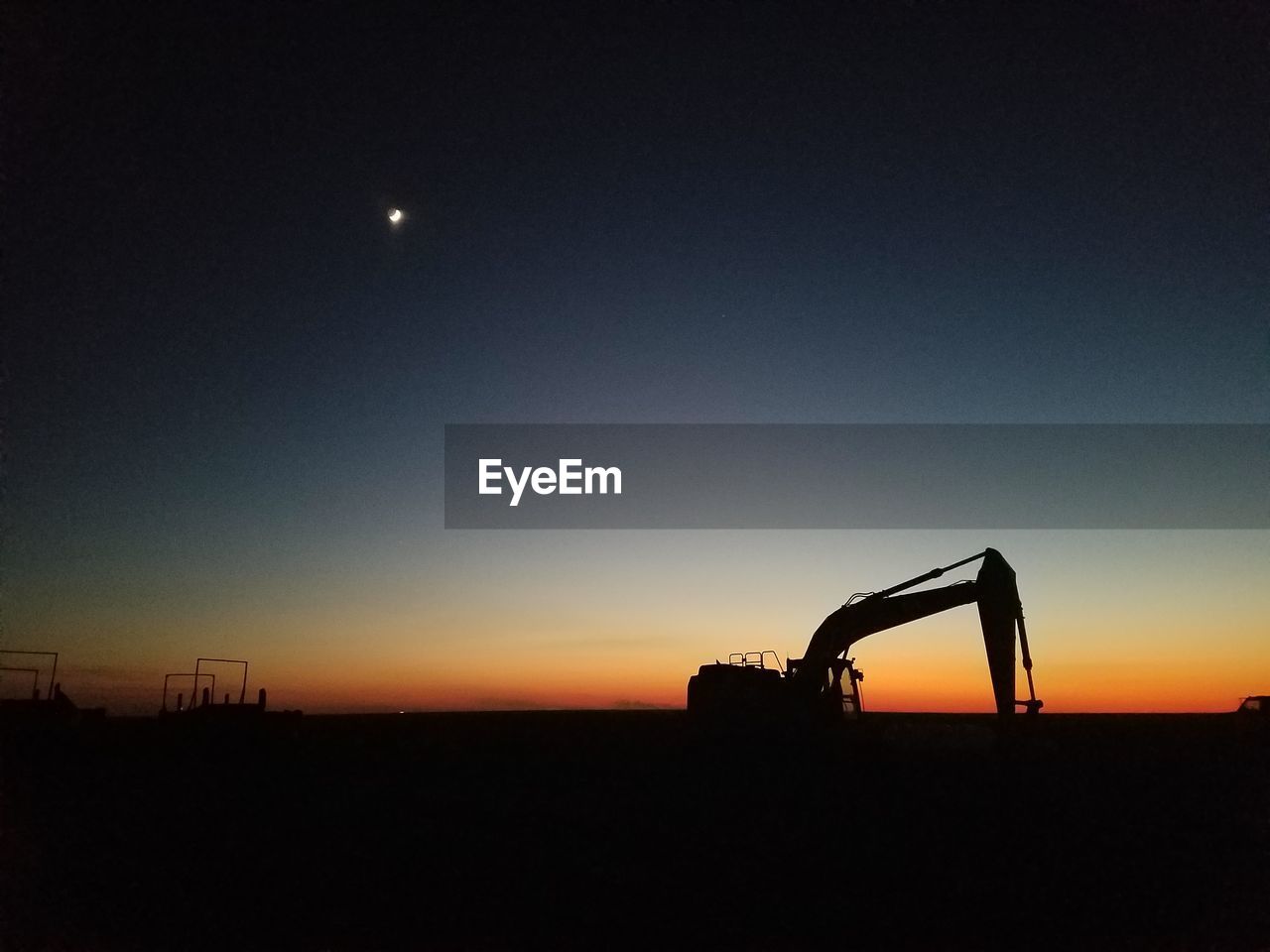 Silhouette bulldozer on field against sky during sunset