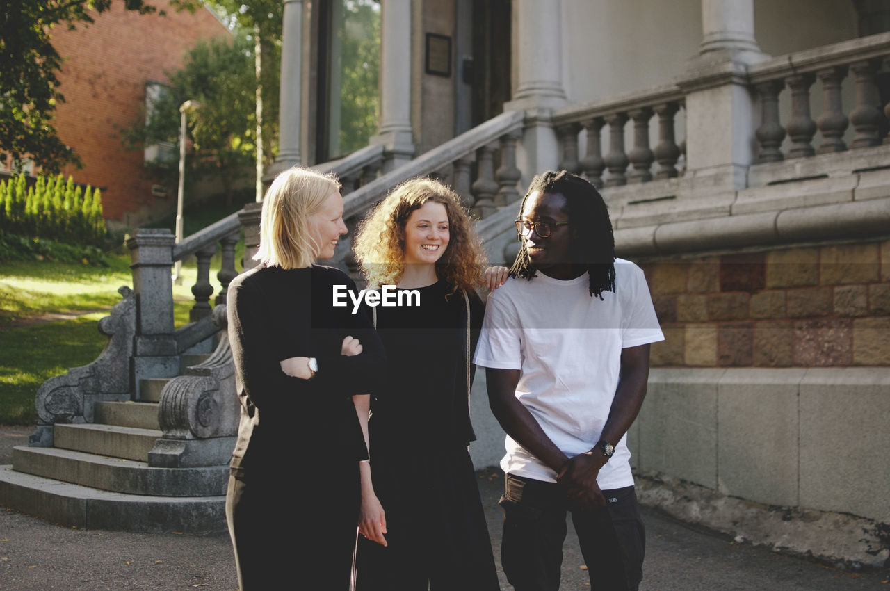 Multi-ethnic male and female students talking while walking by university