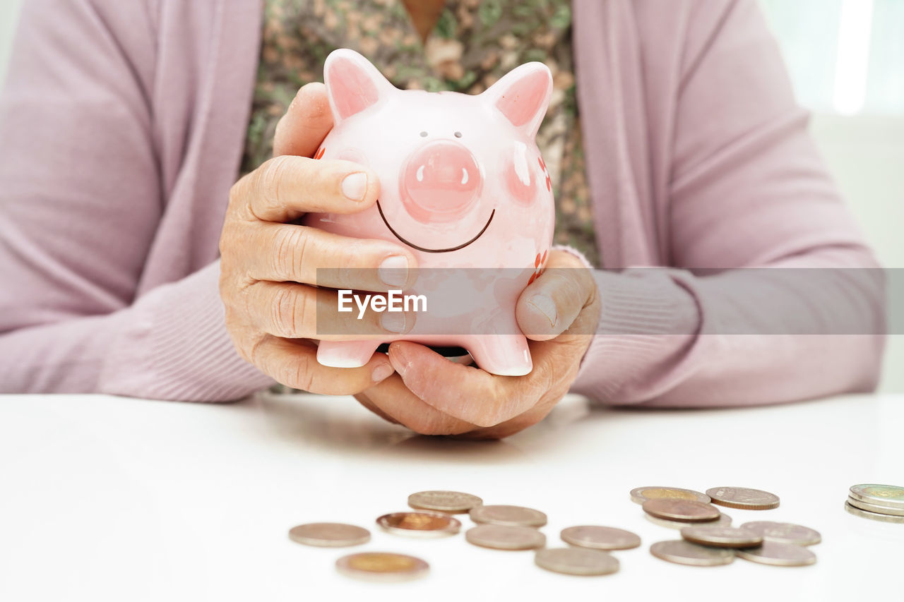 midsection of woman inserting coin in piggy bank