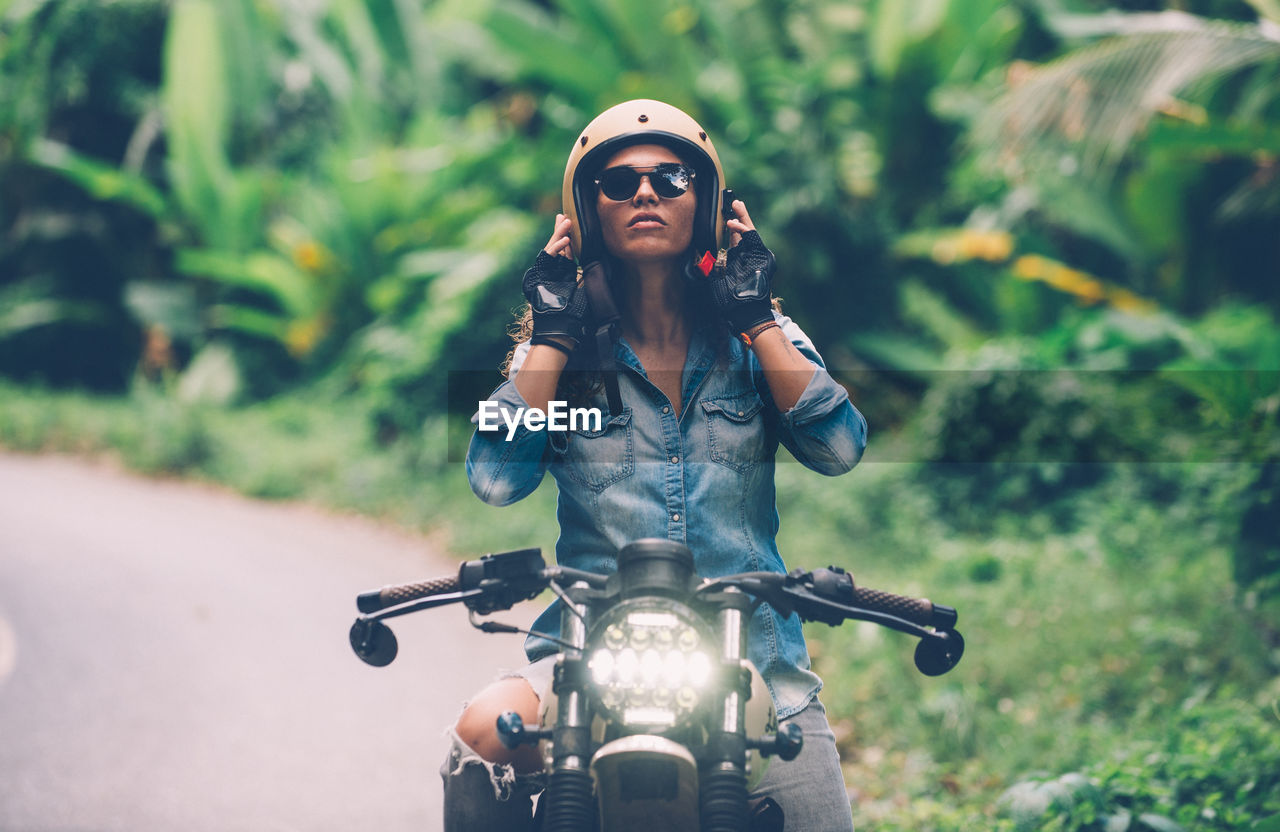 Woman wearing helmet while sitting on motorbike on road