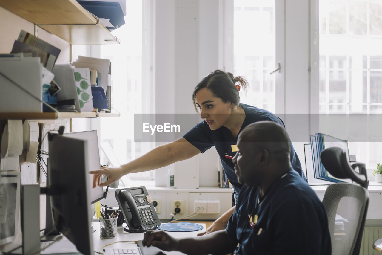 Female nurse pointing over computer while discussing with colleague at hospital